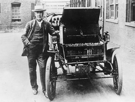 Thomas Edison poses with his first electric car, the Edison Baker, and one of its batteries, c.1895.